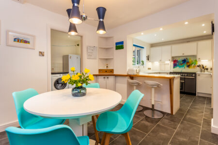 Open plan white kitchen diner. Round white dining table with blue chairs