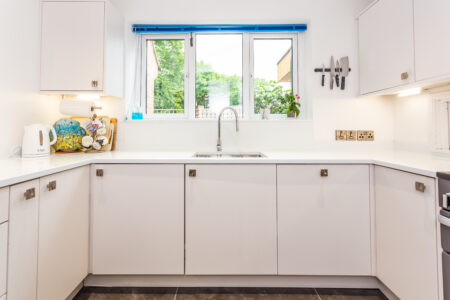 Open plan white kitchen diner. Round white dining table with blue chairs