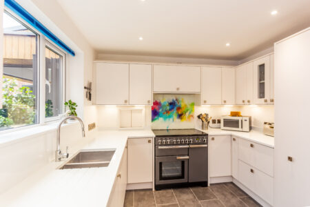 Open plan white kitchen diner. Round white dining table with blue chairs