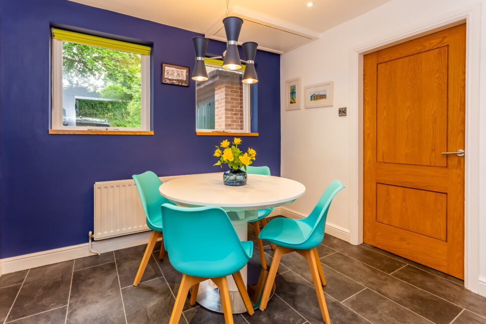 Open plan white kitchen diner. Round white dining table with blue chairs