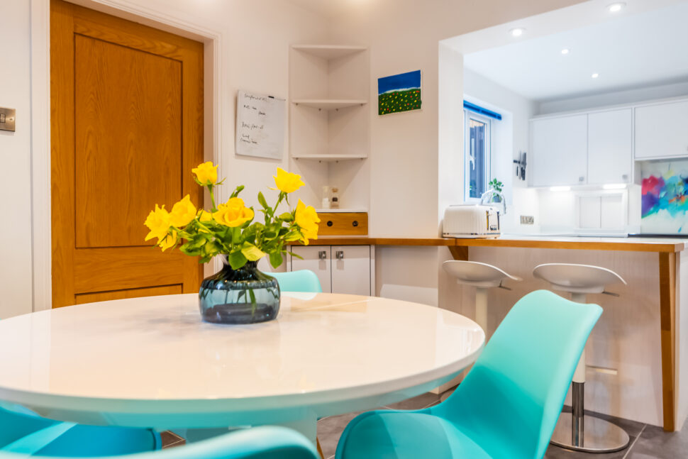 Open plan white kitchen diner. Round white dining table with blue chairs