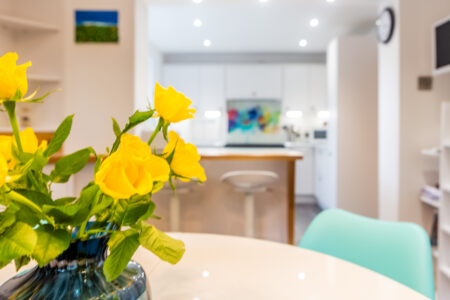 Open plan white kitchen diner. Round white dining table with blue chairs