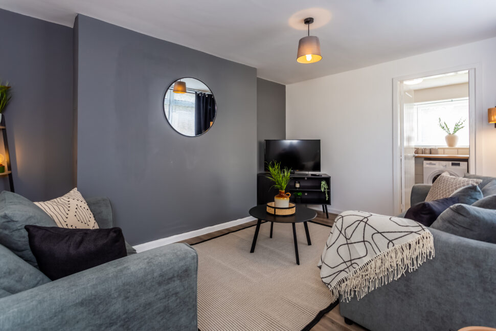 Off white living room with grey feature wall. Black coffee table. Grey curtains. Round mirror