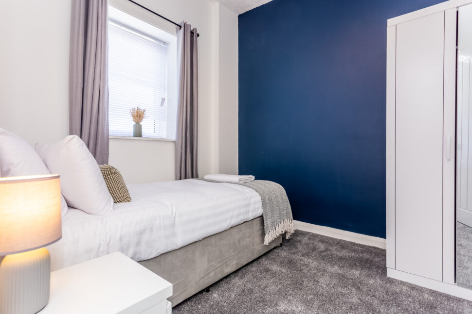 Off white single bedroom. Navy feature wall. Grey accessories