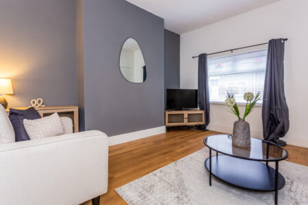 Off white living room. Grey feature wall. Beige Sofas. Black circular coffee table. Large rug