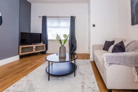 Off white living room. Grey feature wall. Beige Sofas. Black circular coffee table. Large rug