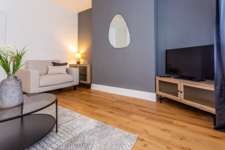 Off white living room. Grey feature wall. Beige Sofas. Black circular coffee table. Large rug