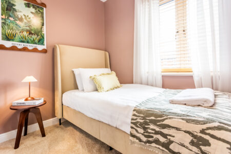 Sulking room pink single beige fabric bed. Walnut side table. White wardrobe. Green accessories