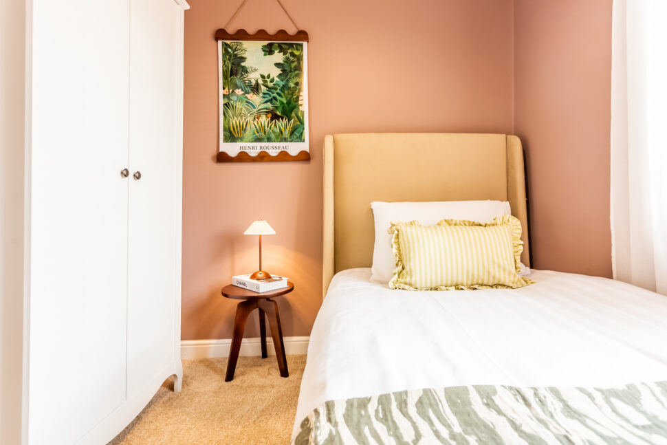 Sulking room pink single beige fabric bed. Walnut side table. White wardrobe. Green accessories