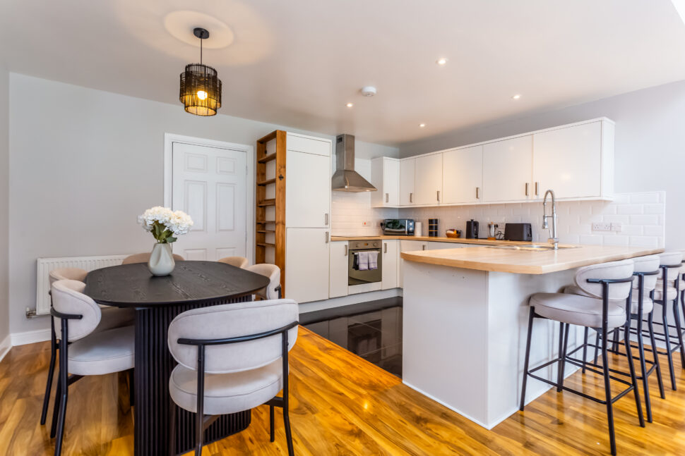 White kitchen with peninsular island with oak worktops. Black dining table