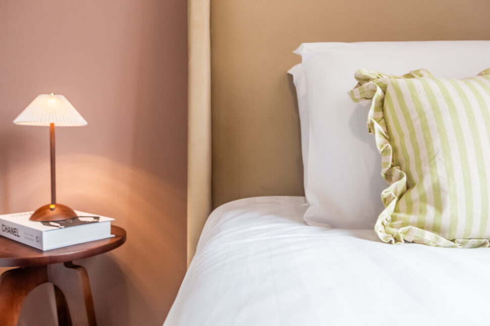 Sulking room pink single beige fabric bed. Walnut side table. White wardrobe. Green accessories