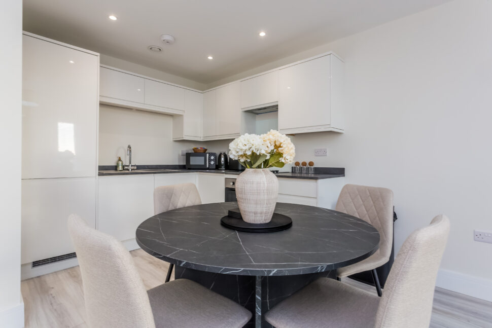 A luxurious open plan kitchen and dining area in neutral tones. The dining table has a beautiful flower display in the centre. high-quality short term accommodation
