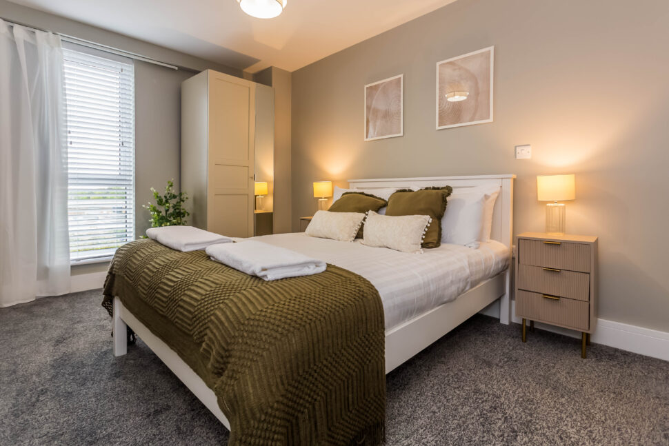 Image shows an ambiently lit cosy bedroom. The colours are earthy and muted shades of olive green. high-quality short term accommodation