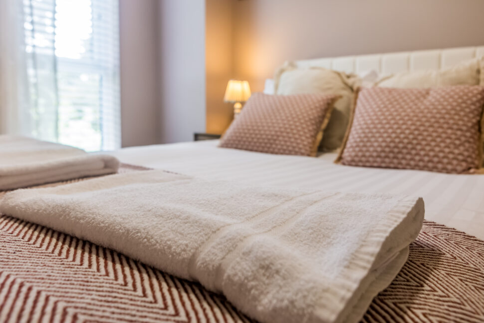 Toast Stays, close up looking across the bed diagonally, showing coordinated scatter cushions, throw with guest towels neatly folded on top